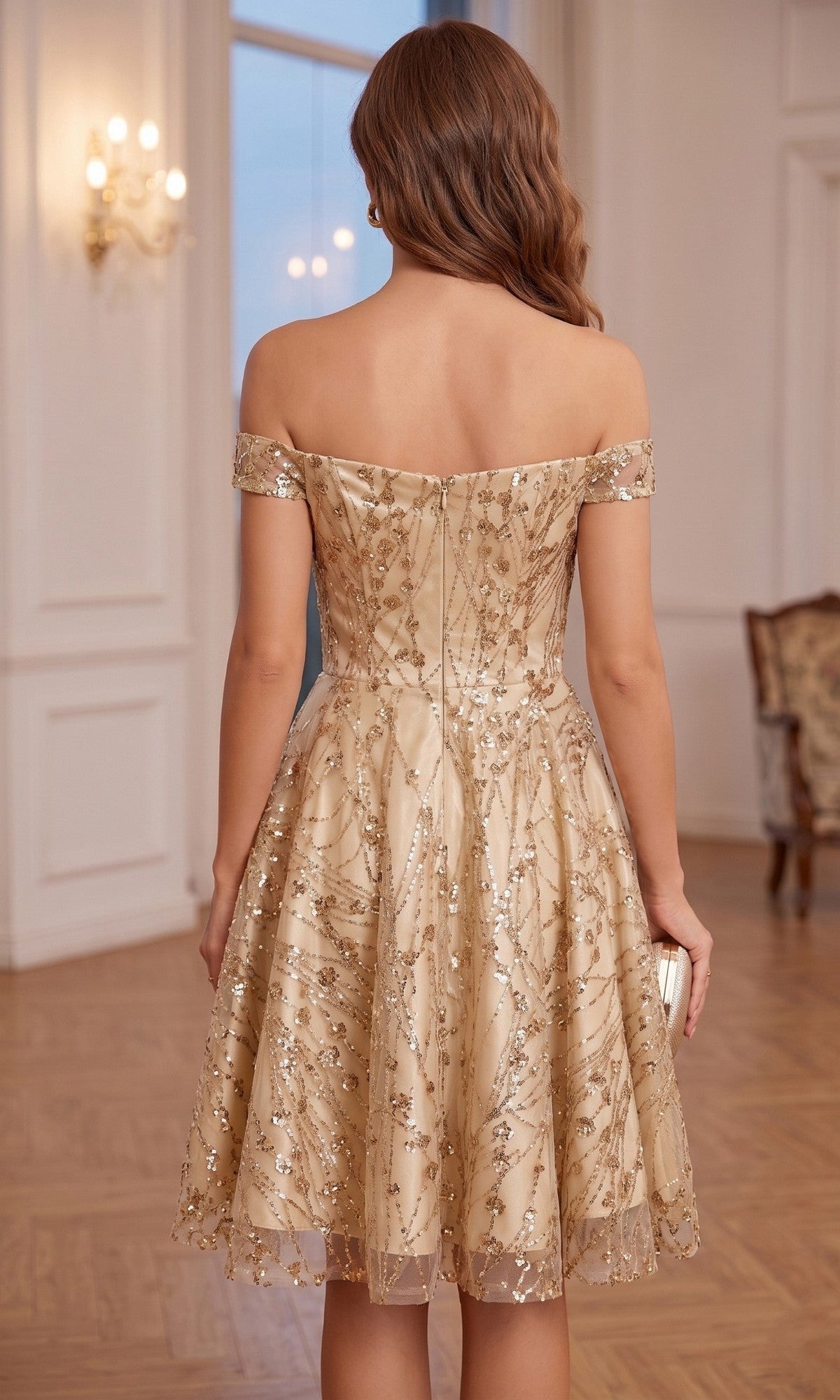 A woman with wavy brown hair stands in an elegant room, facing away from the camera, wearing the Chicas 4021 Short Homecoming Dress—an off-the-shoulder, sweetheart neckline, knee-length dress with gold embroidery.